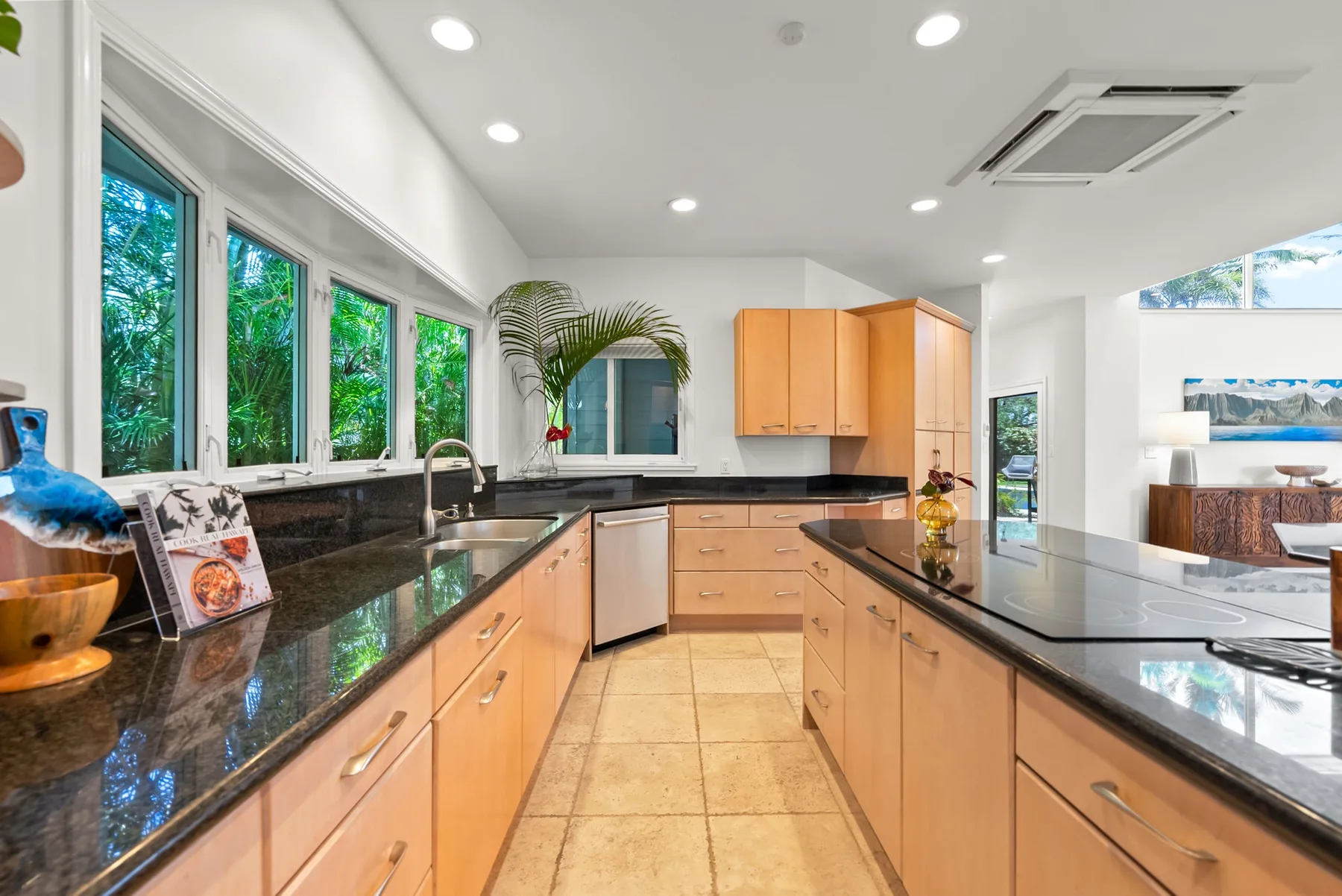 Una cocina luminosa con gabinetes de madera, encimeras oscuras y ventanas grandes.