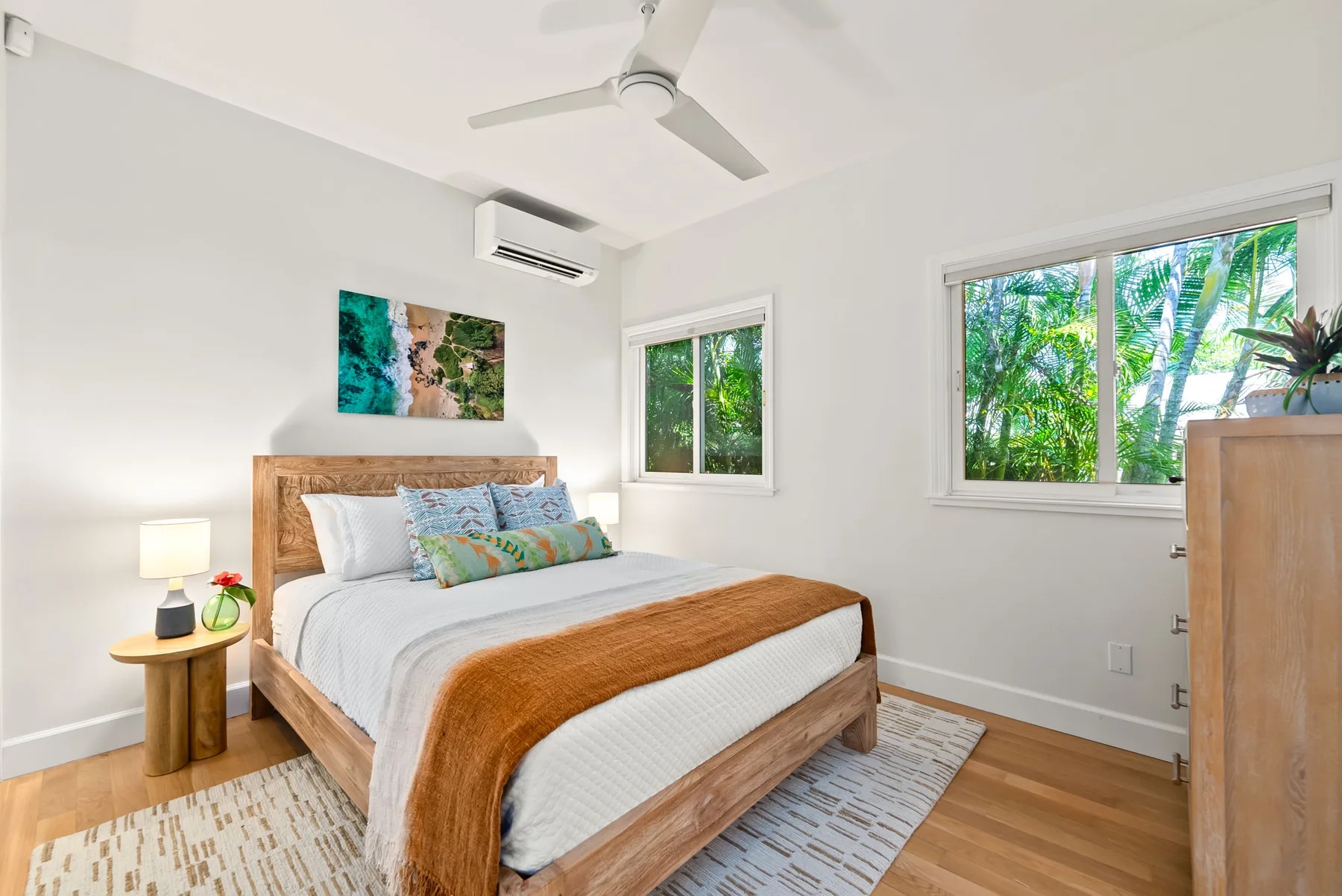 Un dormitorio con cama, mesita de noche y ventanas con vistas a la vegetación.