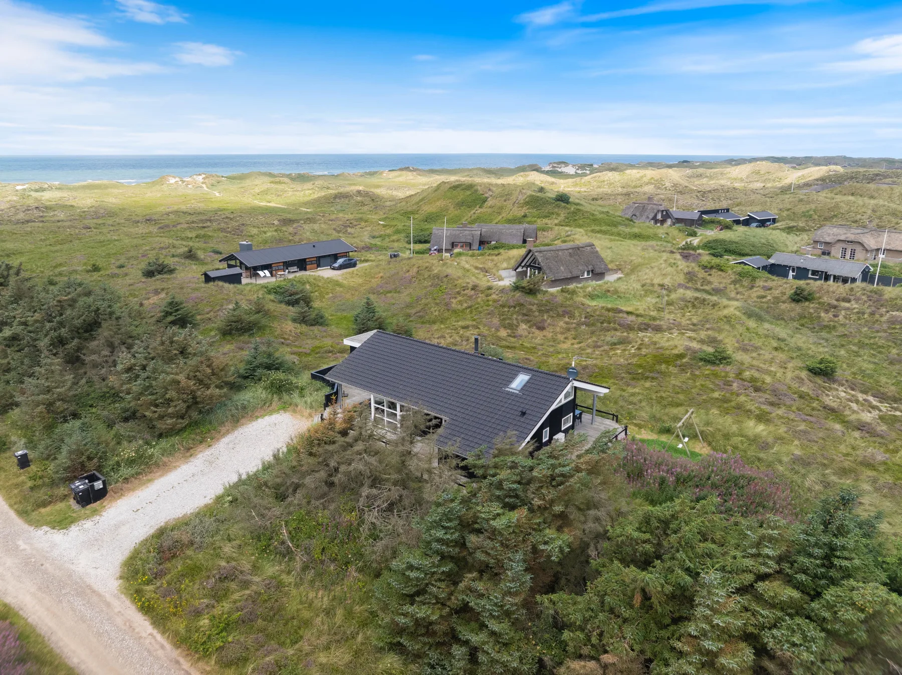 Aerial view of scattered houses among grassy dunes near the coast.