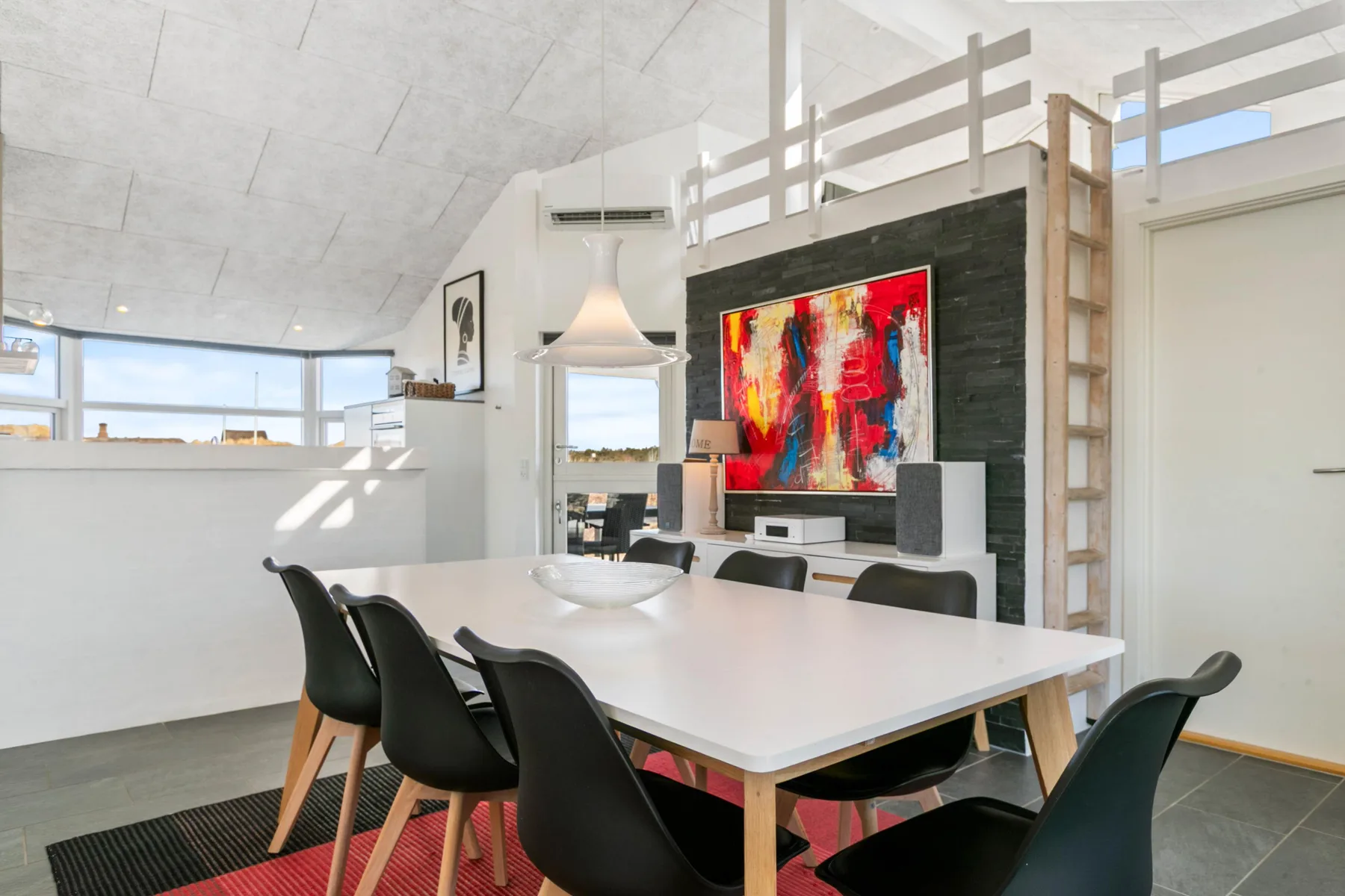 A bright dining area with a long table, dark seating, and colorful artwork.