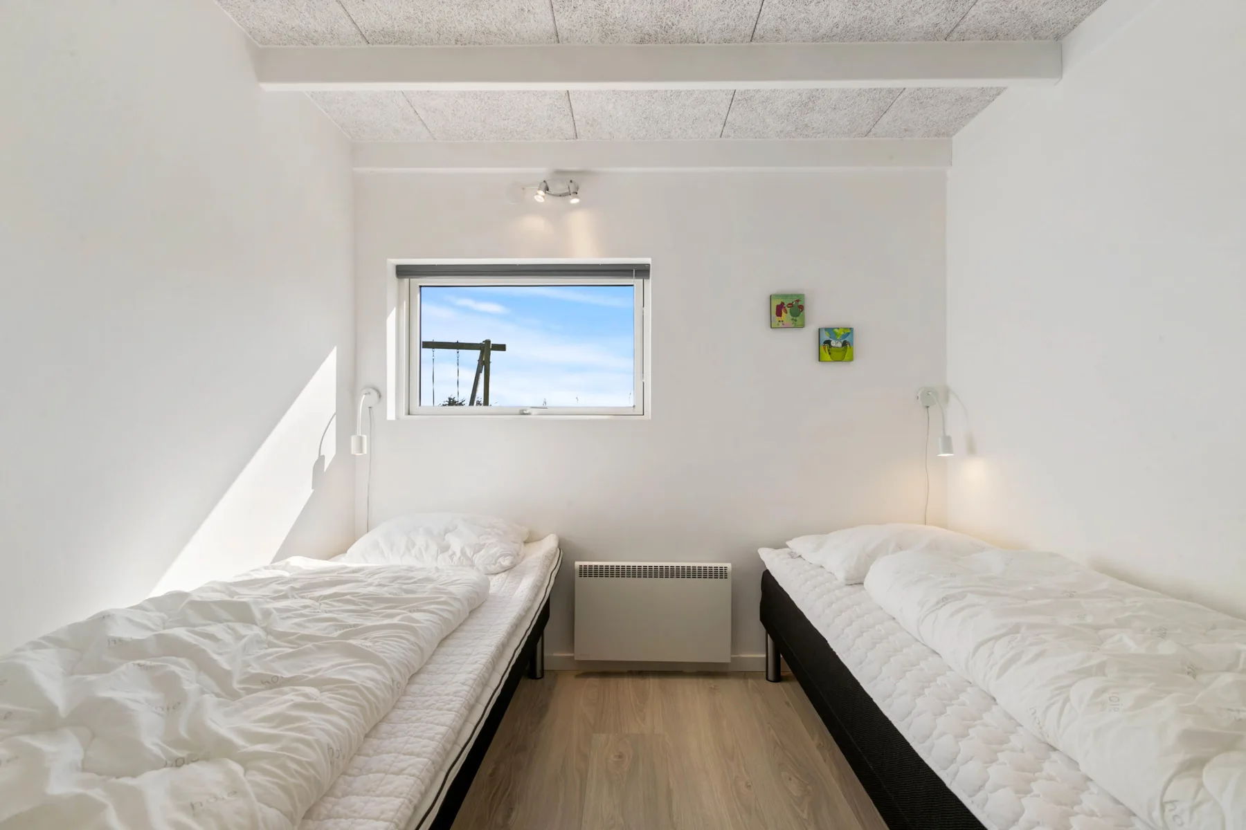 A bright bedroom with two single beds beneath a window.