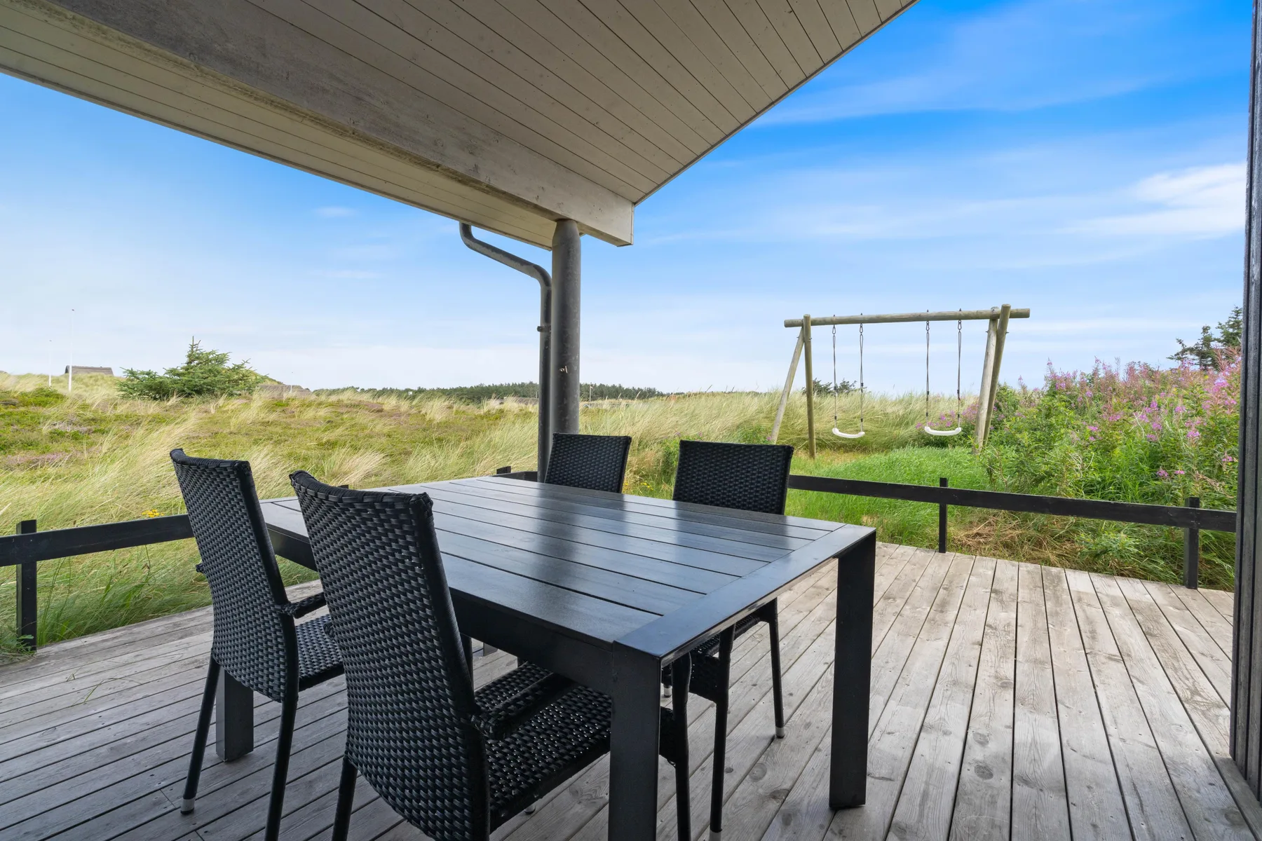 A covered outdoor dining area with a table and seating overlooks grassy dunes.