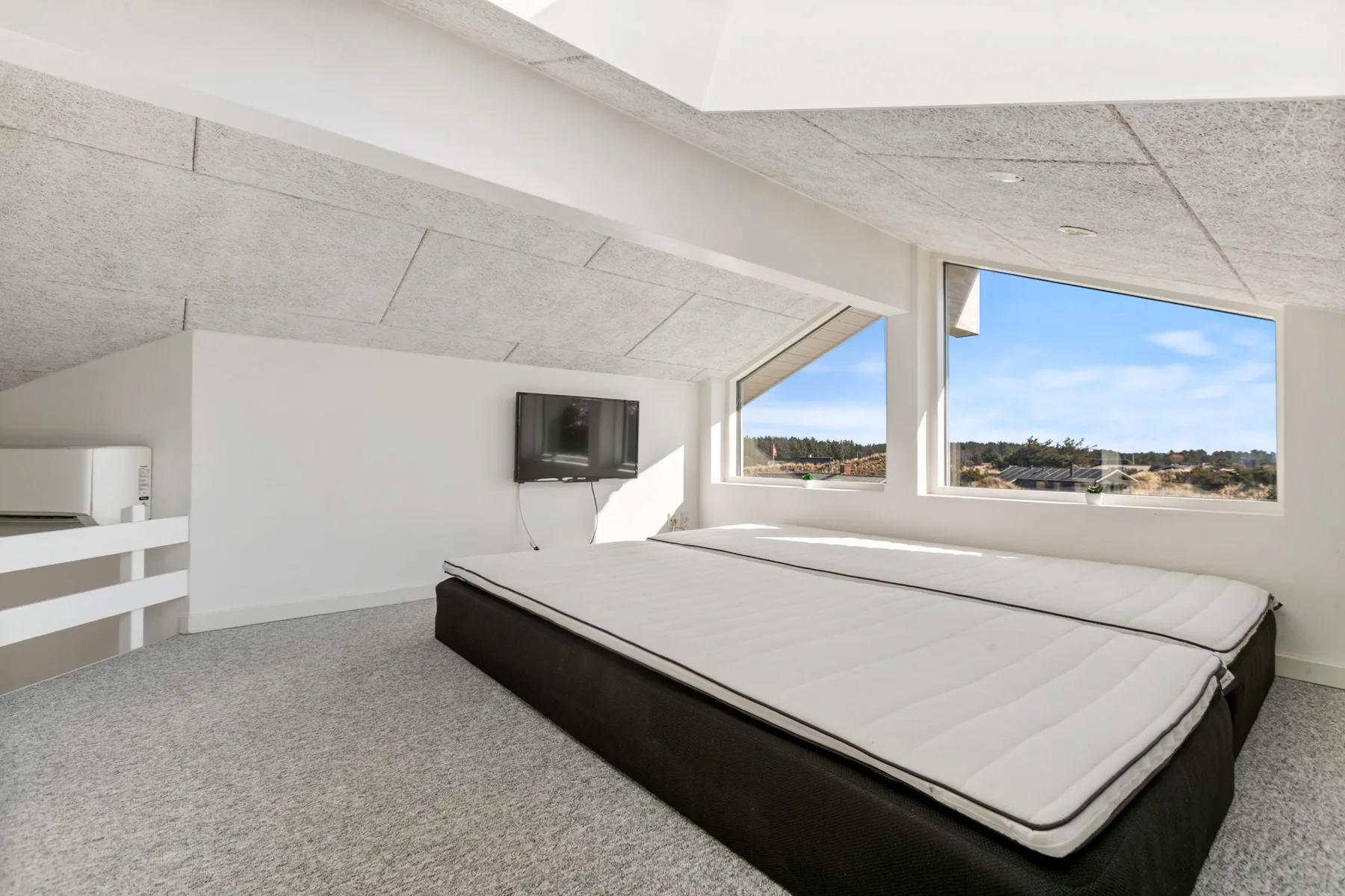 A bright bedroom with a large bed and wide windows overlooking the landscape.