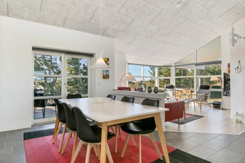 A bright open-plan dining and living area with large windows and a dining table.
