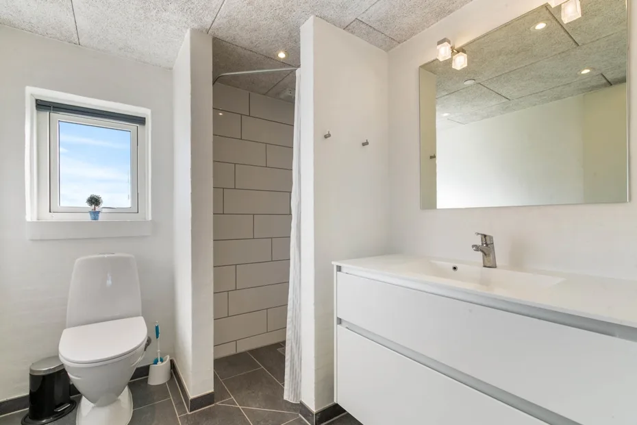 A bathroom with a vanity, mirror, toilet, and tiled shower.
