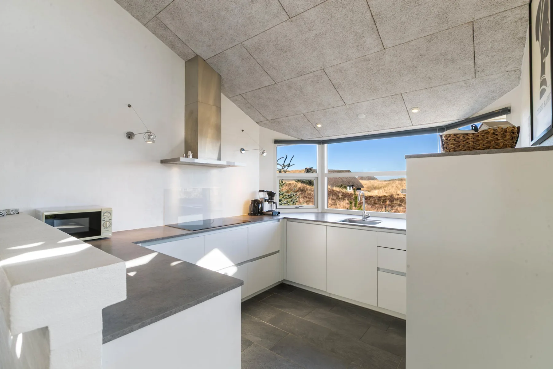 A modern kitchen with white cabinetry, a dark countertop, and wide windows.