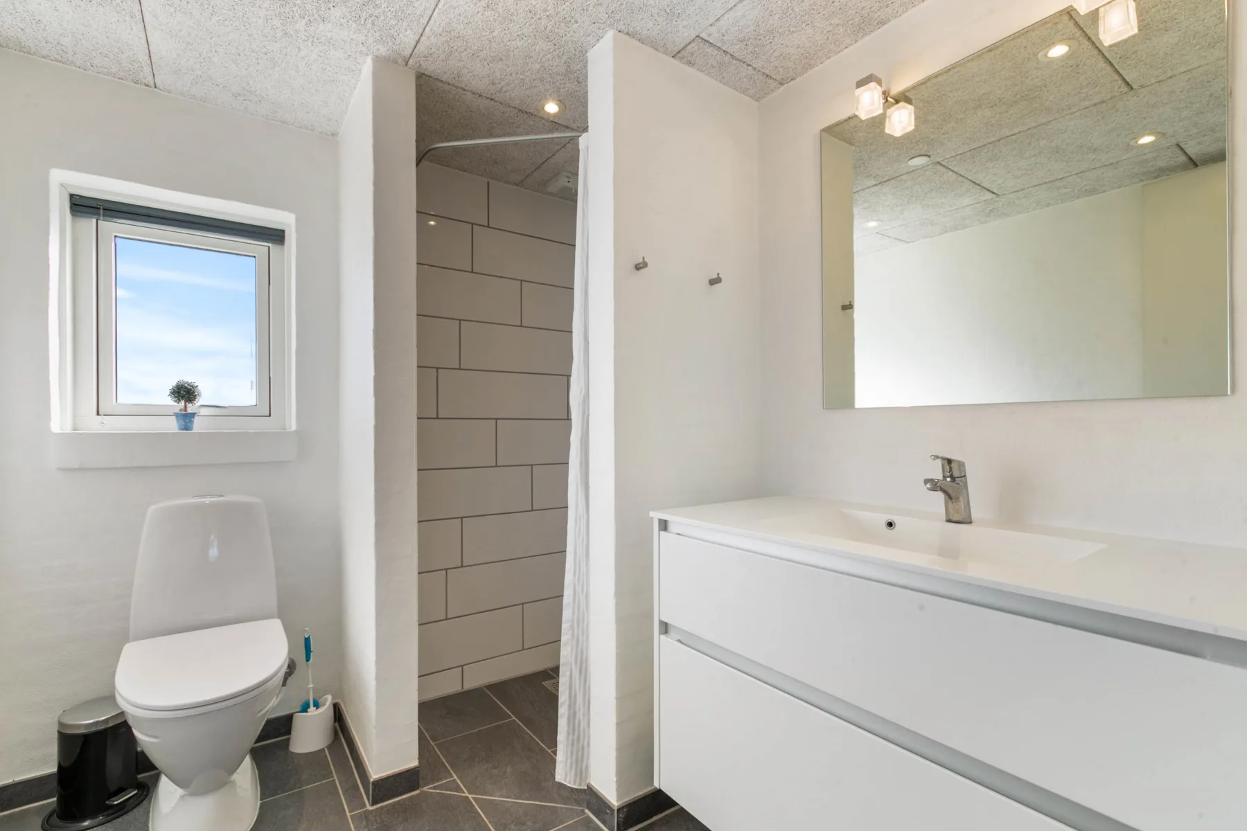 A bathroom with a vanity, mirror, toilet, and tiled shower.