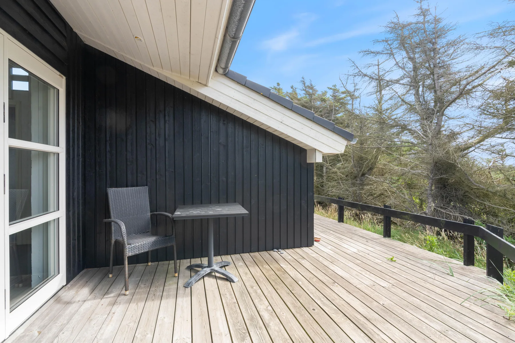 An outdoor deck beside a dark-sided building has seating and a small table.