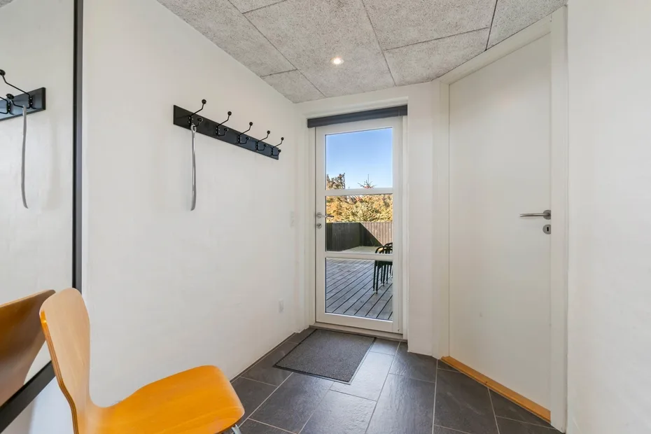 A bright entryway with wall hooks, a glass door, and a chair.