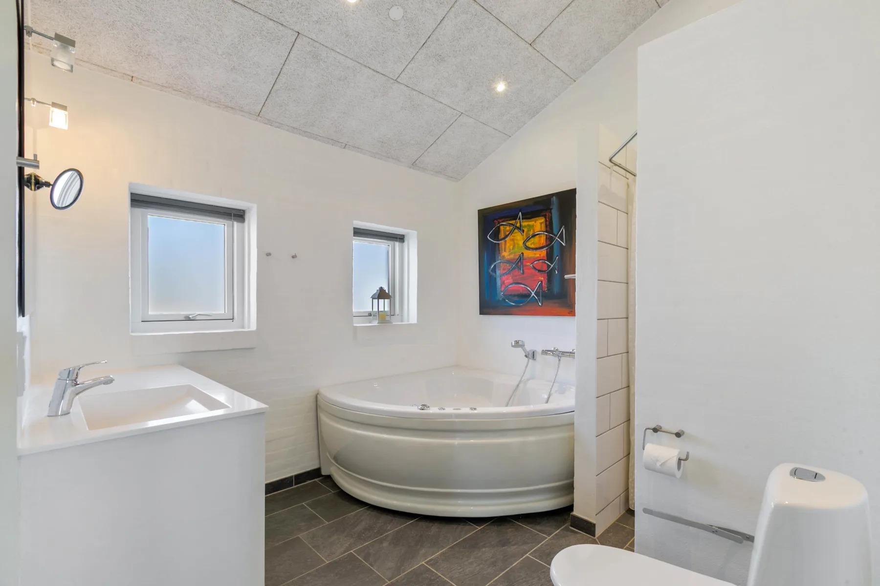 A bright bathroom with a corner bathtub, sink, and windows.