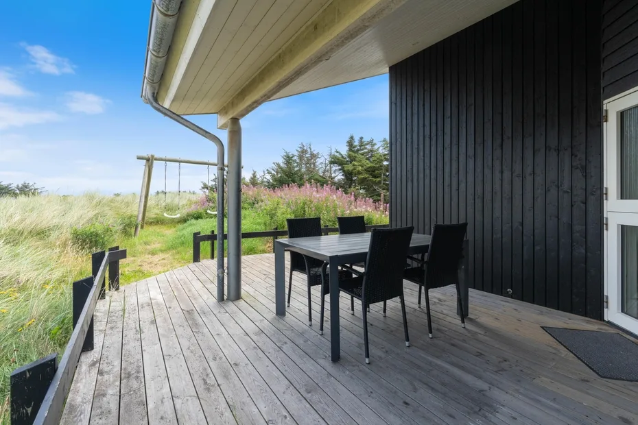 An outdoor dining area sits on a wooden deck beside a dark-sided house.