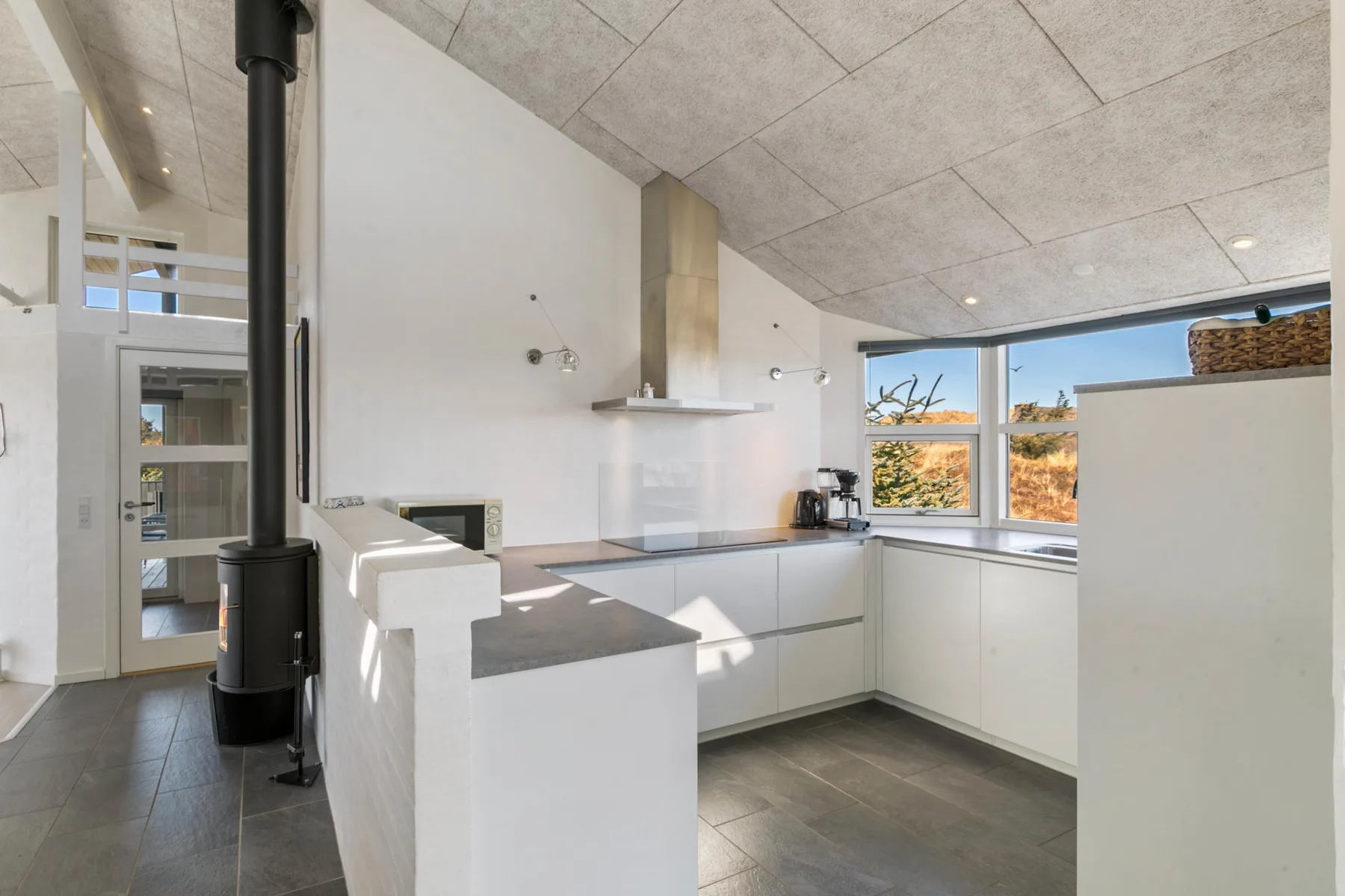 A modern kitchen with white cabinets, a central island, and large windows.