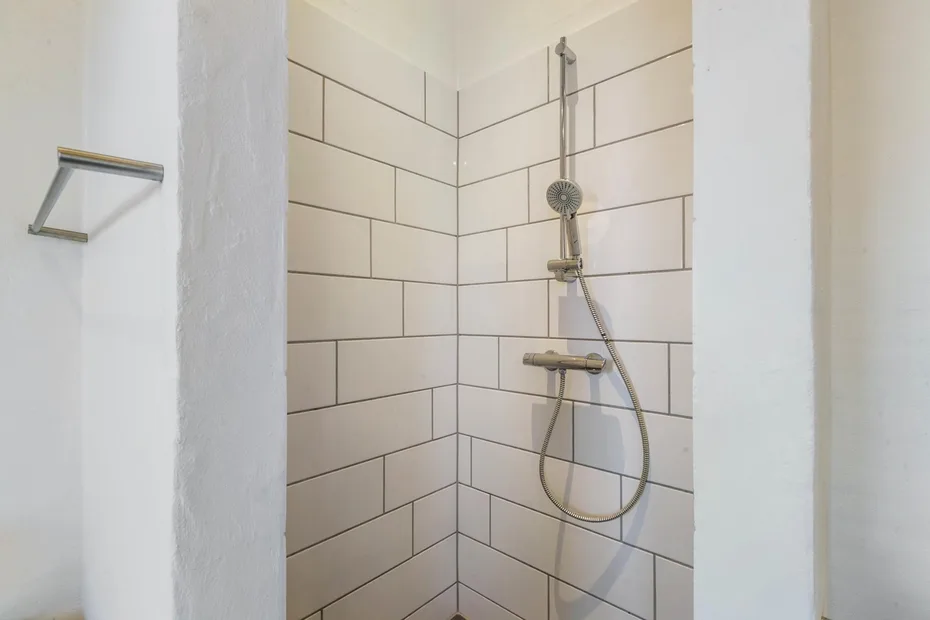 A tiled shower with a handheld showerhead and wall-mounted fixtures.