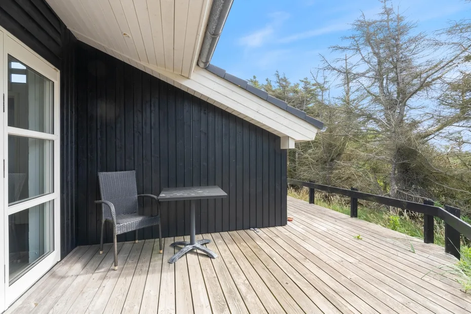 A wooden deck beside a dark-sided building has a chair and small table.