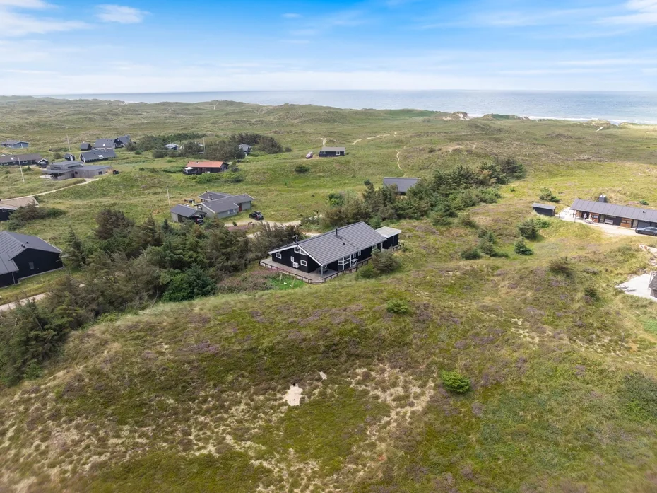 Aerial view of scattered houses among grassy dunes near the coast.