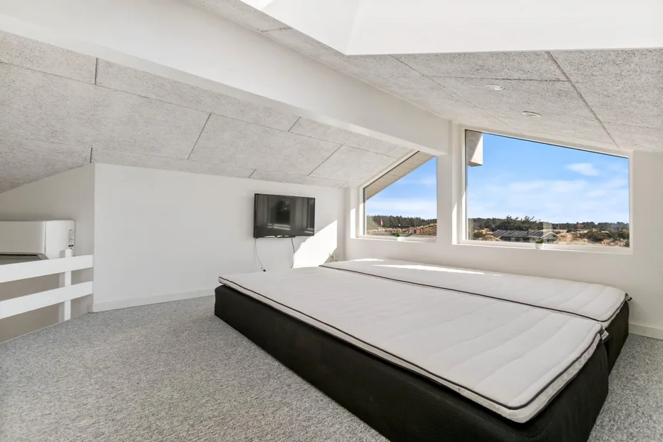 A bright bedroom with a large bed and wide windows overlooking the landscape.