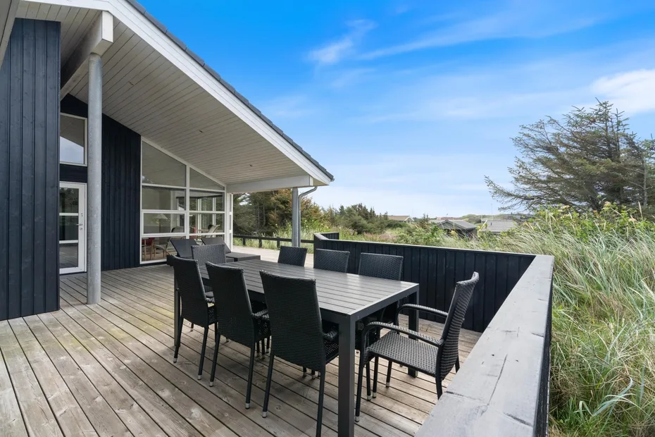 An outdoor dining area sits on a wooden deck beside a house.