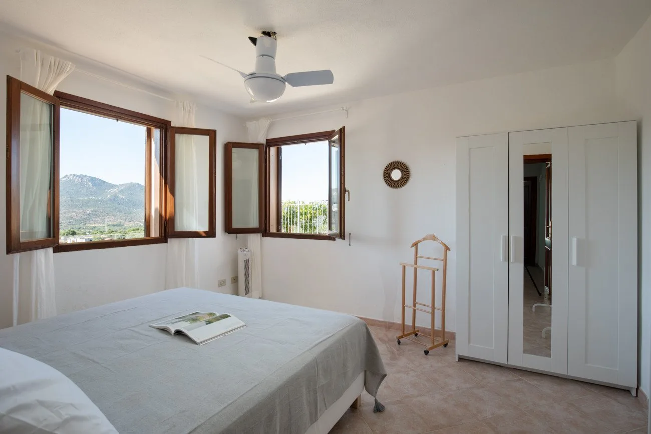 A bright bedroom with a bed, open windows, and a wardrobe.