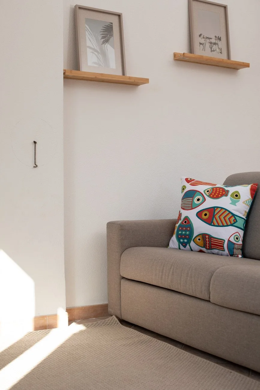 A bright living room corner with a sofa and a colorful patterned cushion.