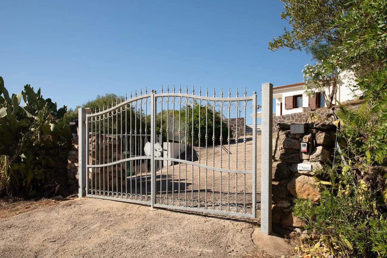 A closed metal gate stands at the entrance to a gravel driveway.