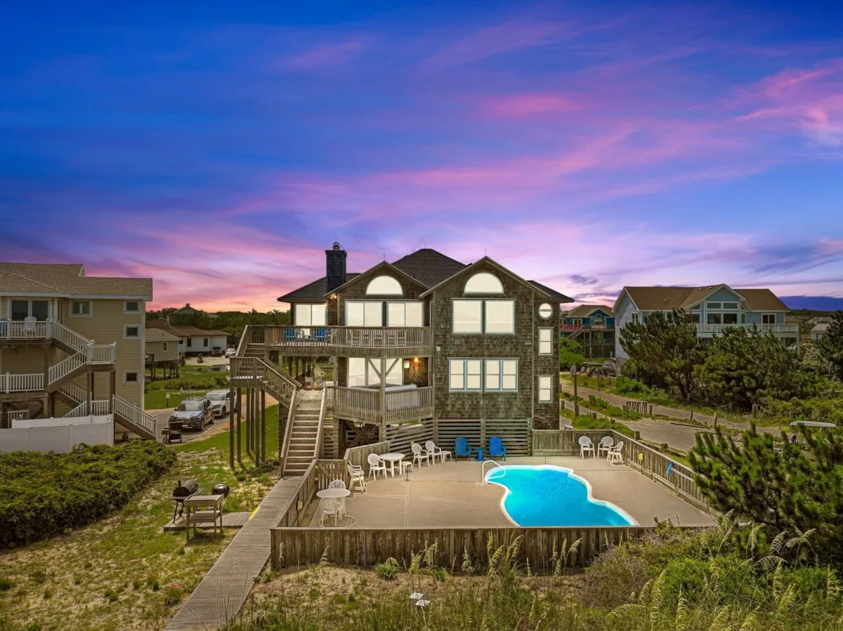 Una casa grande da a una piscina al aire libre bajo un cielo colorido al atardecer.