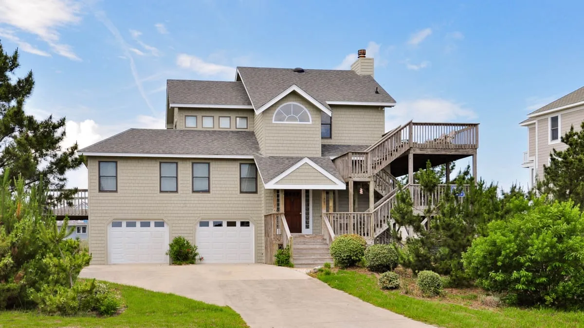 A large house with a driveway, two garage doors, and an elevated deck.