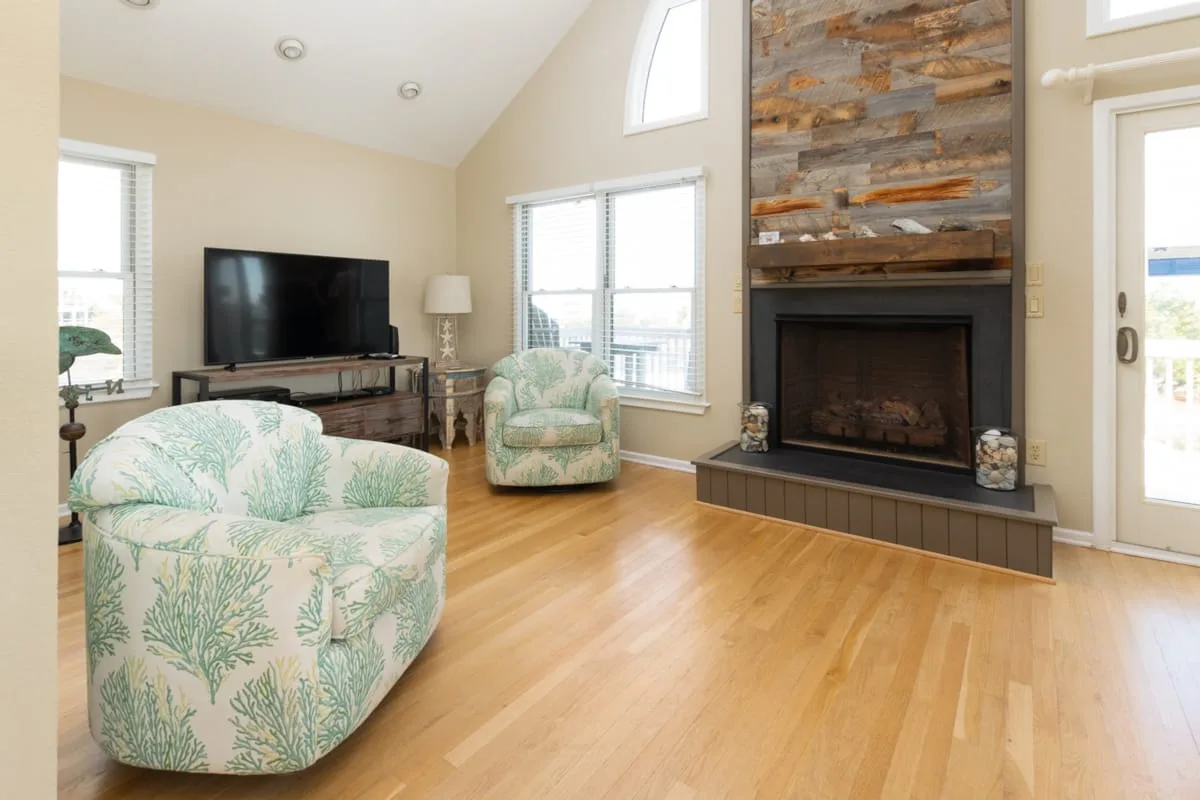 A bright living room with patterned seating, a television, and a fireplace.