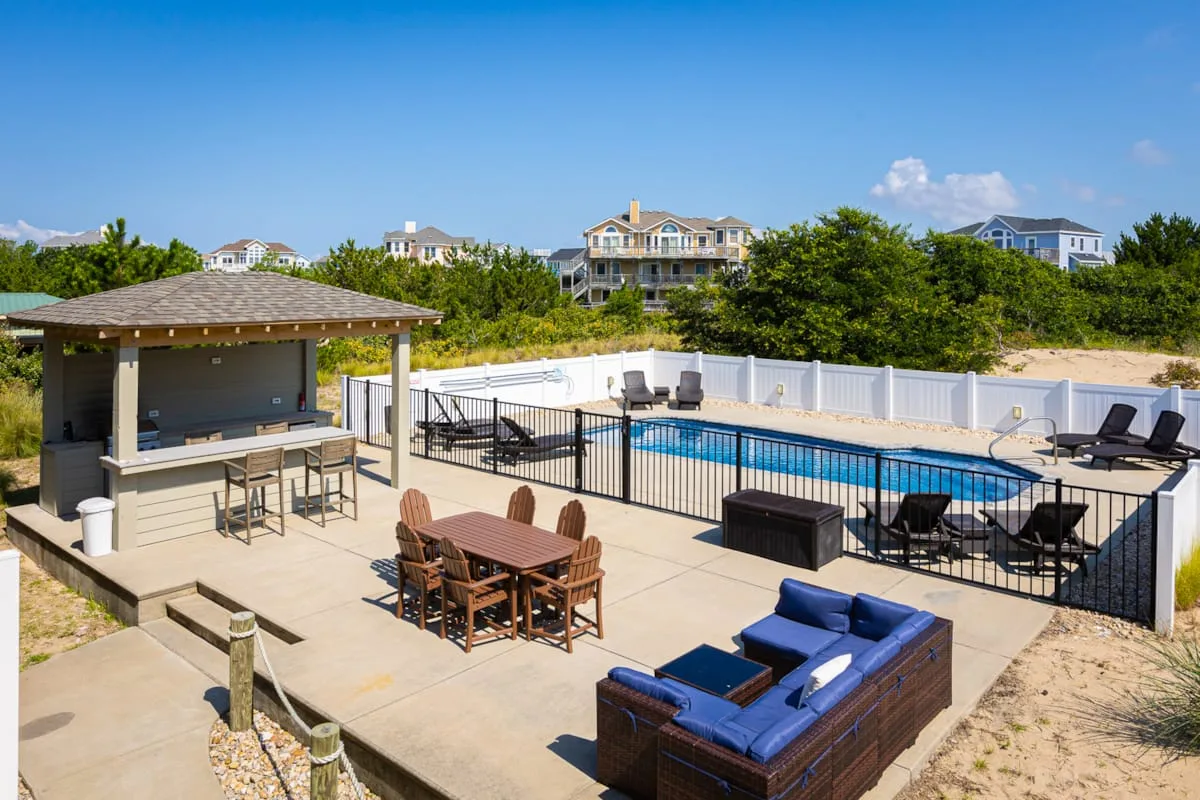 An outdoor pool area has patio seating and a covered bar.