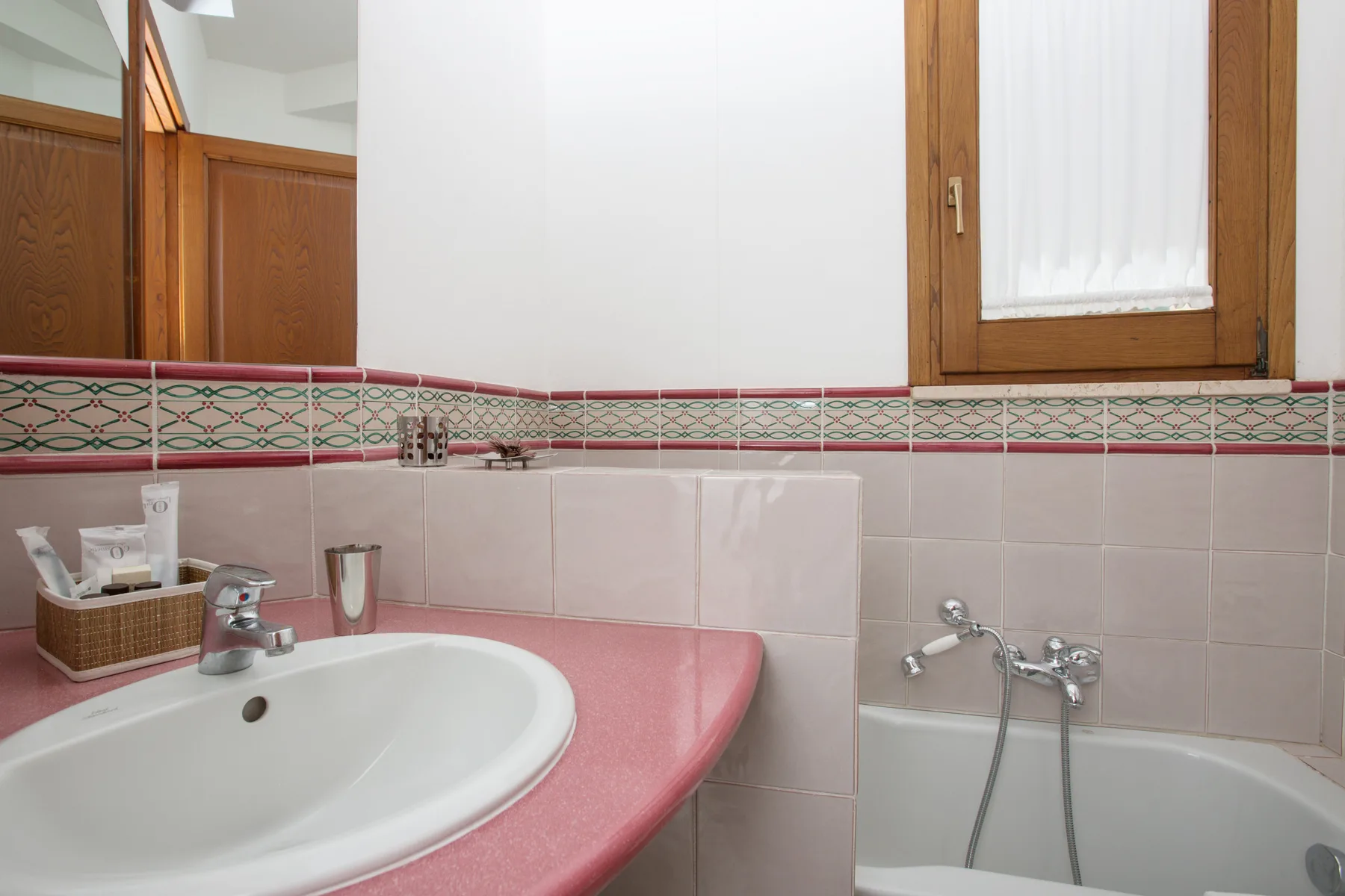 Un lavabo y una bañera están debajo de una ventana con marco de madera.