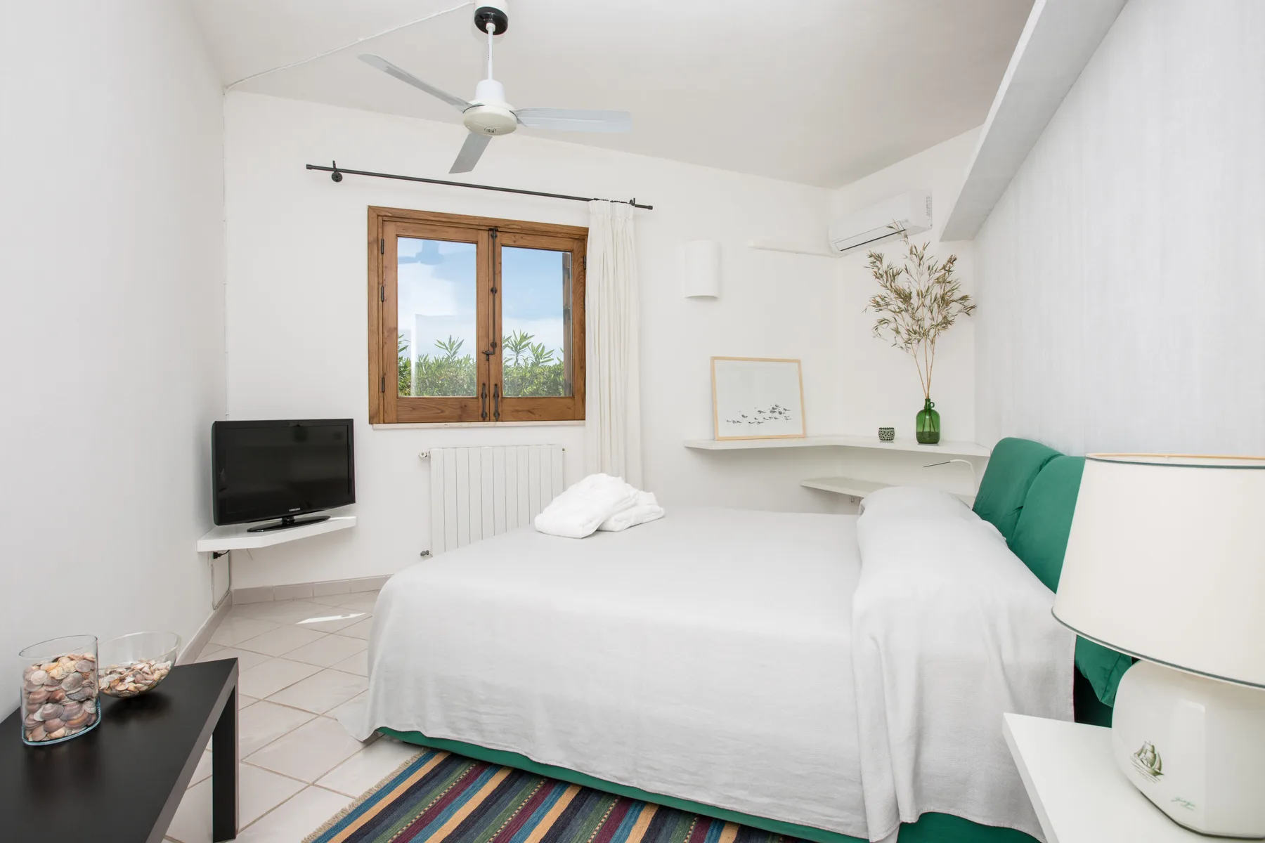 Un dormitorio luminoso con una cama blanca, cabecero verde y ventana con marco de madera.