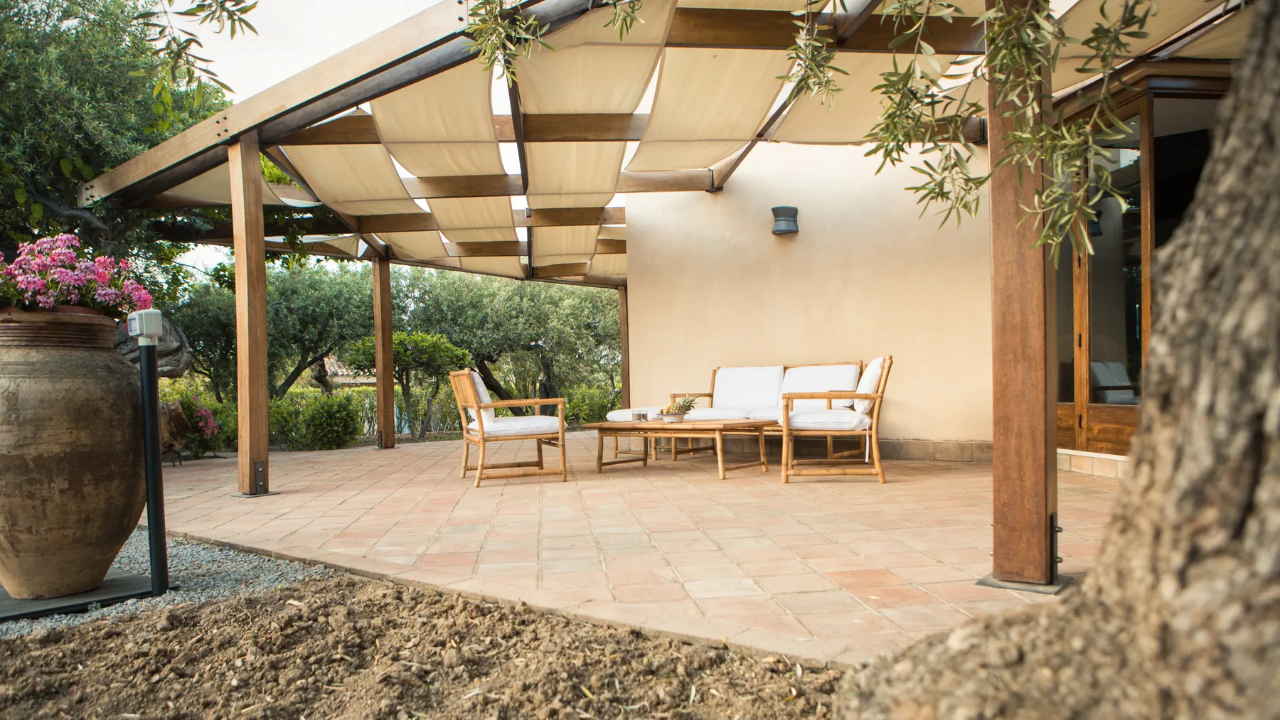 Un patio de baldosas con asientos al aire libre bajo una pérgola de madera y una cubierta de tela.
