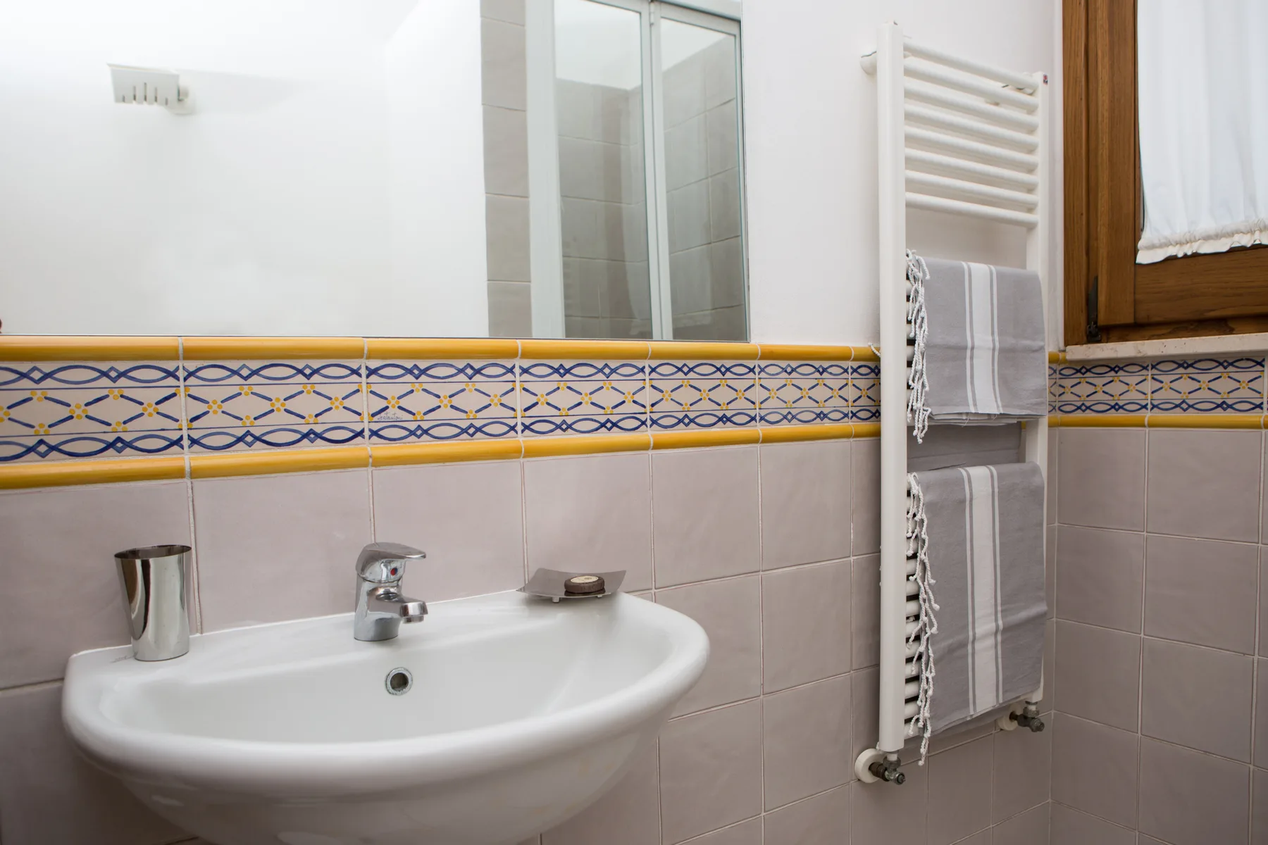 Un baño alicatado con lavabo blanco, espejo y radiador toallero.