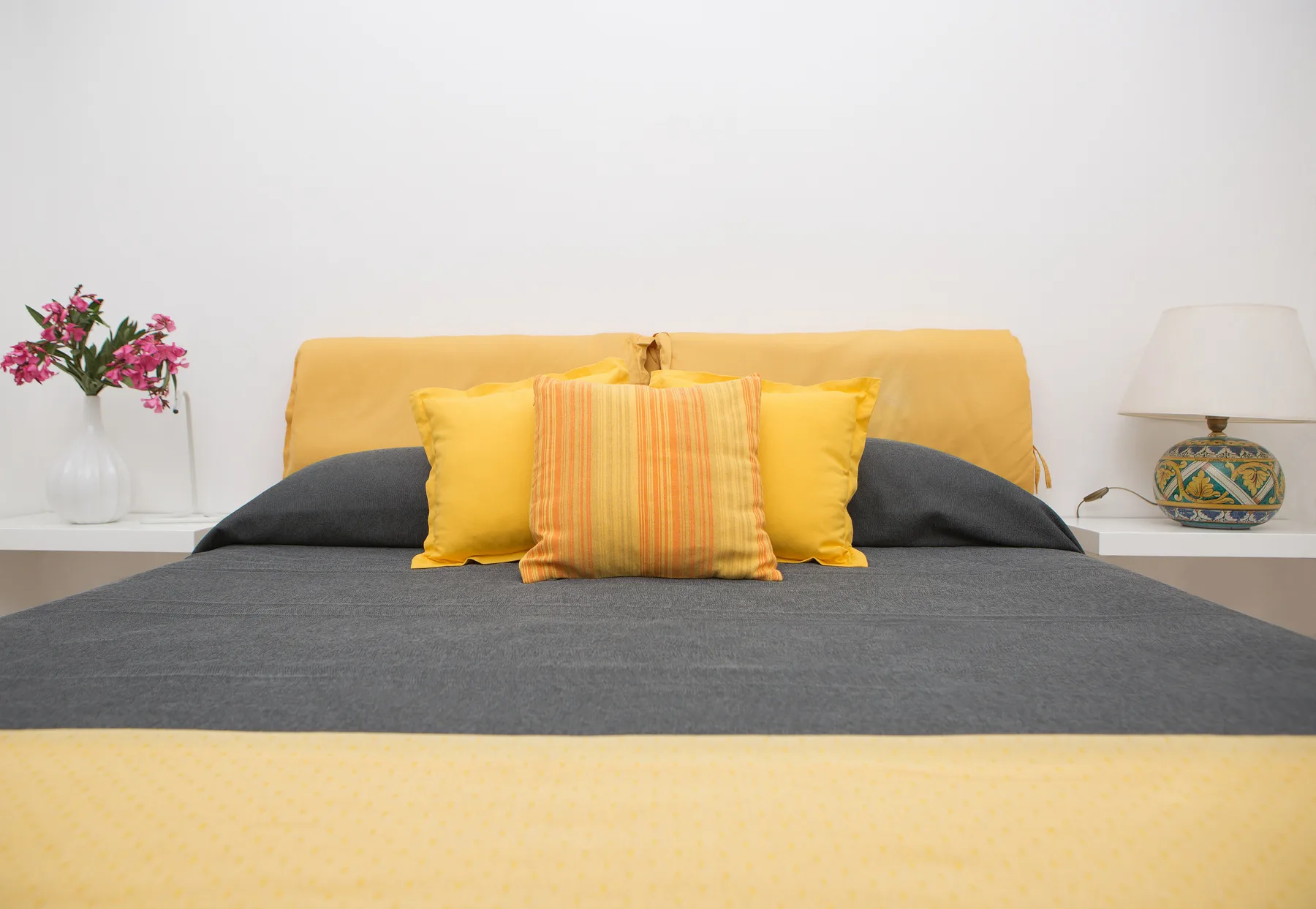 Un dormitorio con una cama bien hecha, almohadas amarillas y mesitas de noche.