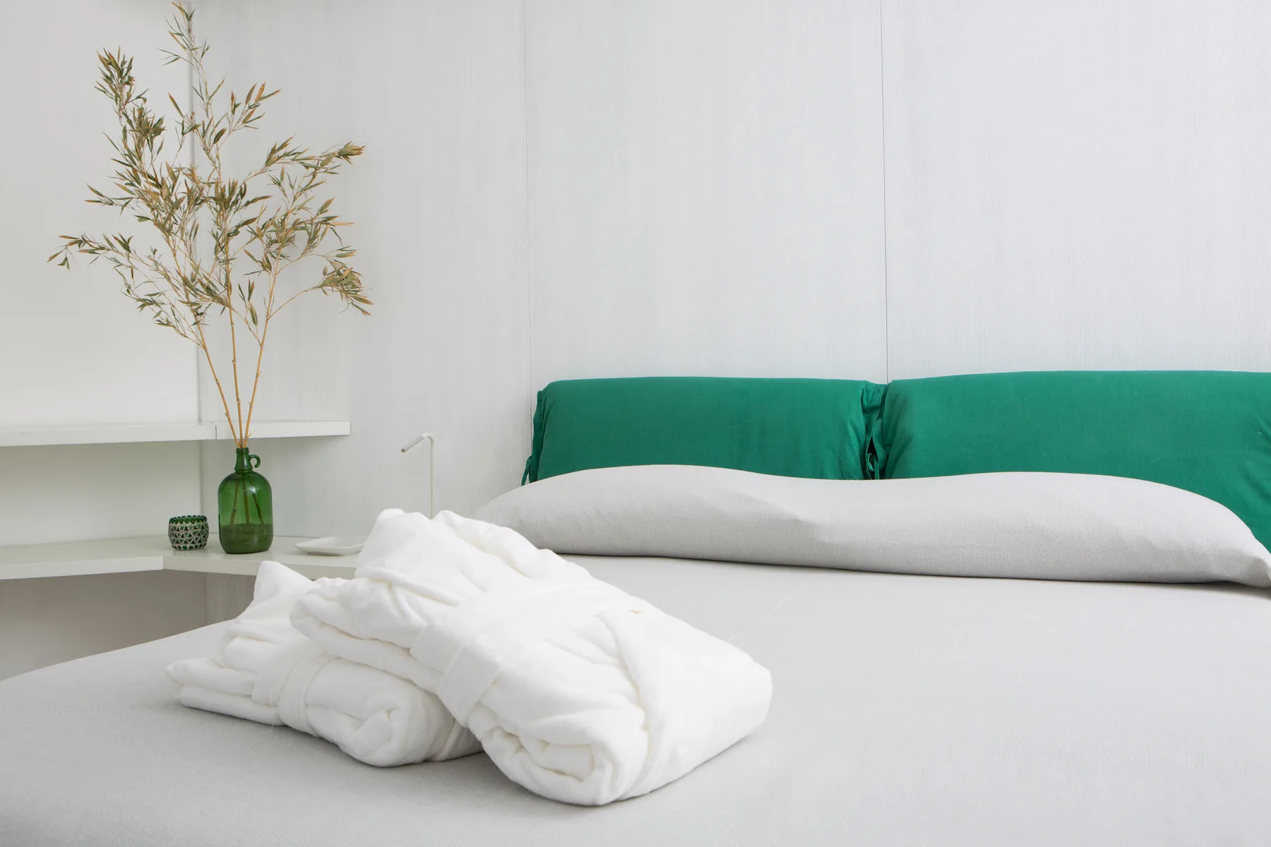 Una cama ordenada con ropa de cama blanca doblada y un cabecero verde.
