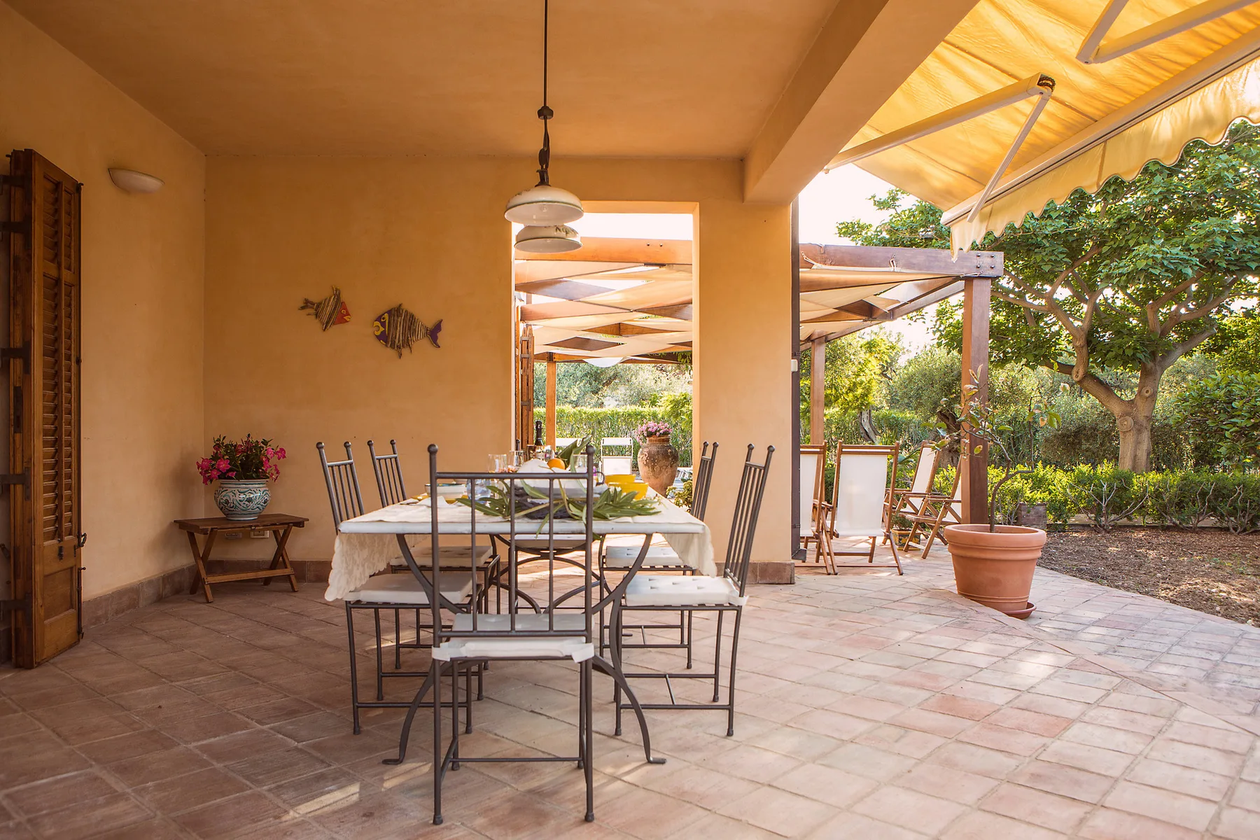 Un comedor cubierto en el patio, con mesa y sillas junto a un jardín.