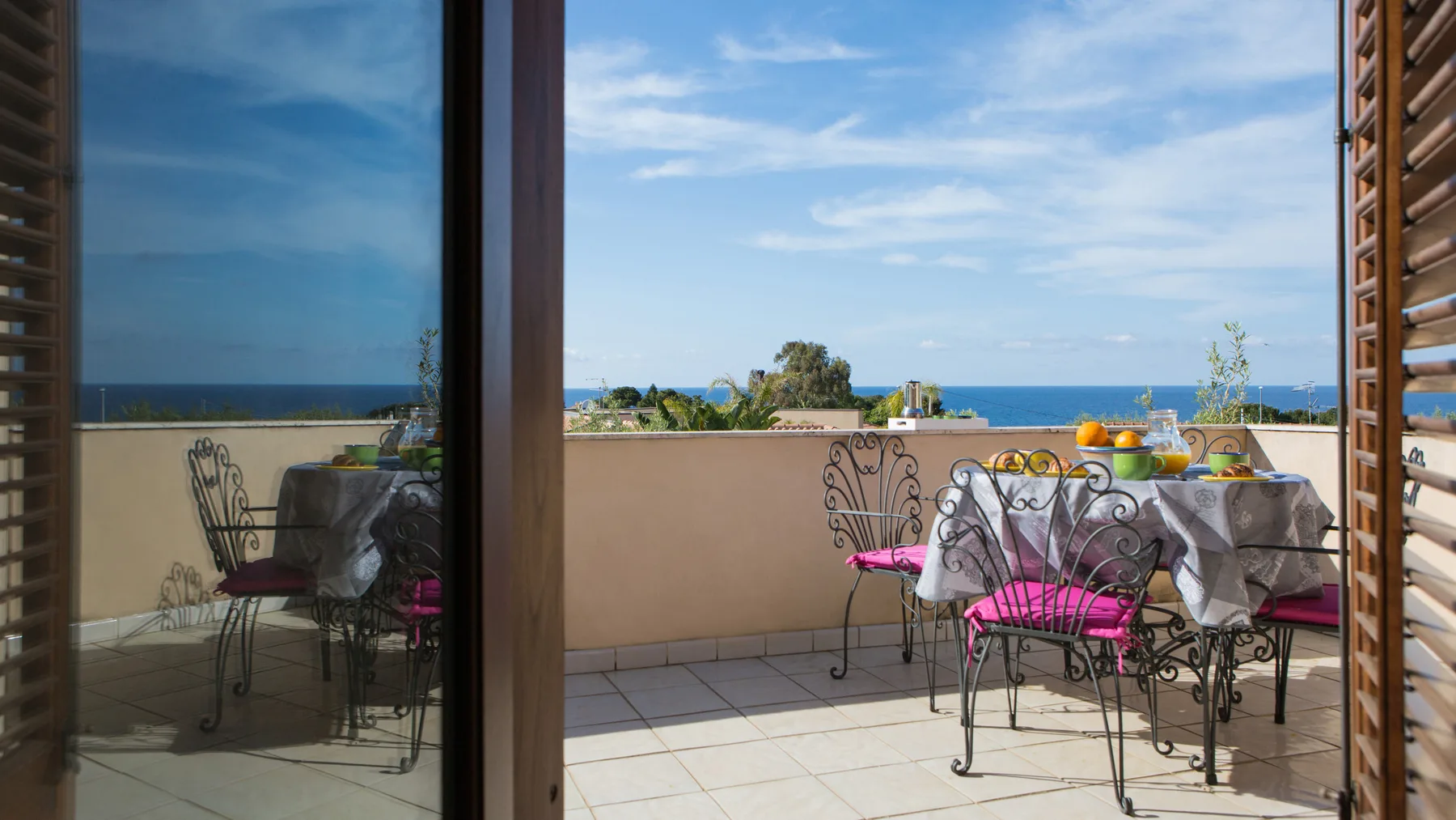 Una terraza exterior con suelo de baldosas tiene una mesa y asientos frente al mar.