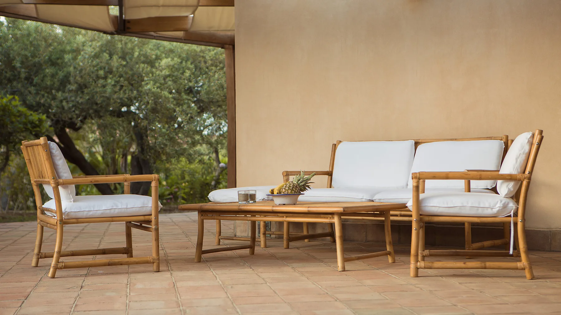 Un patio cubierto tiene asientos acolchados alrededor de una mesa baja, con árboles al fondo.