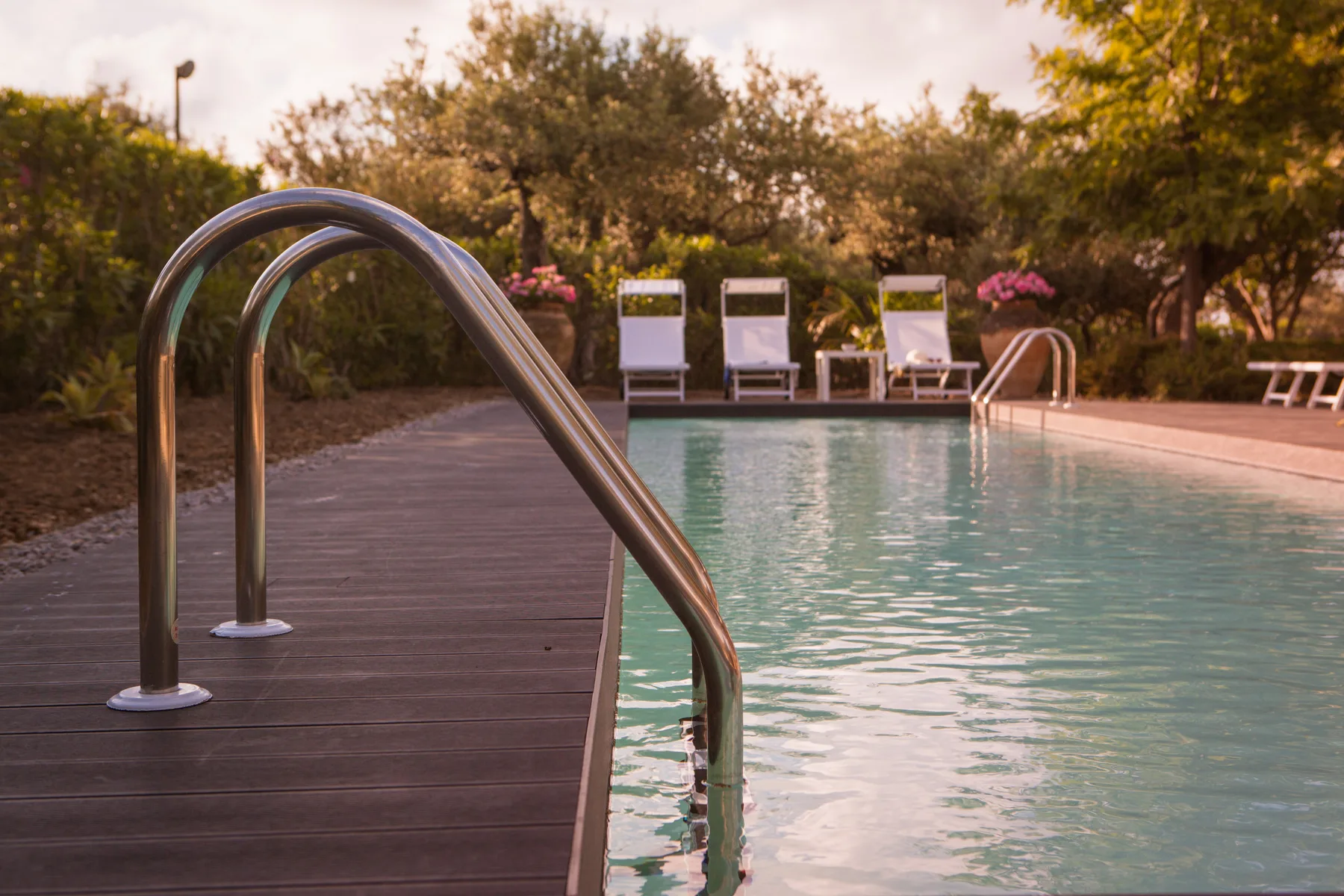 Una piscina al aire libre junto a una terraza de madera y asientos.