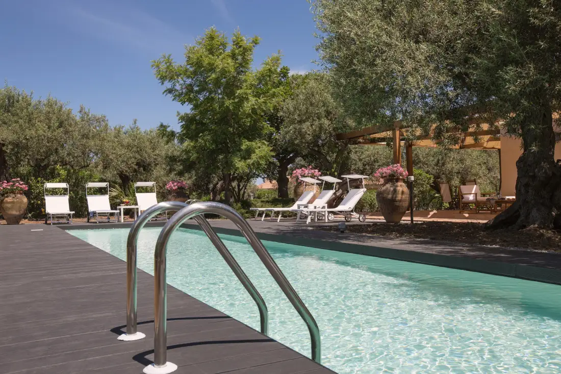 An outdoor swimming pool with lounge chairs beneath the trees.