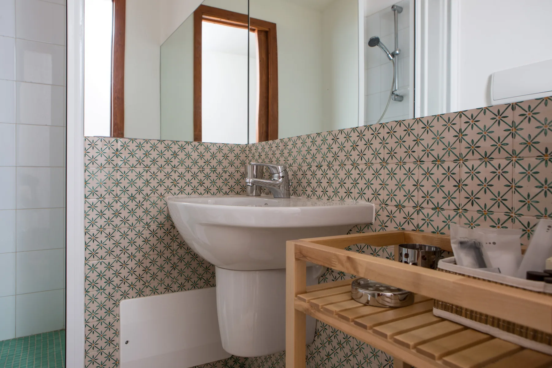 Un baño con lavabo de pared, azulejos estampados y un estante de madera.