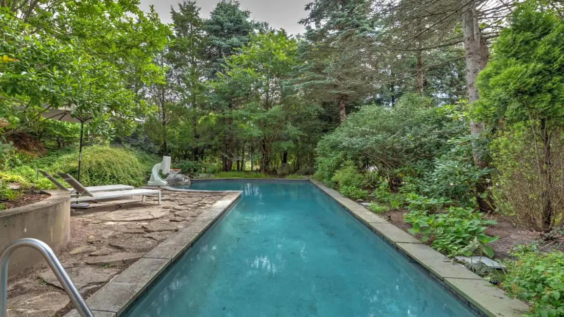 An outdoor swimming pool is surrounded by trees and lush greenery.