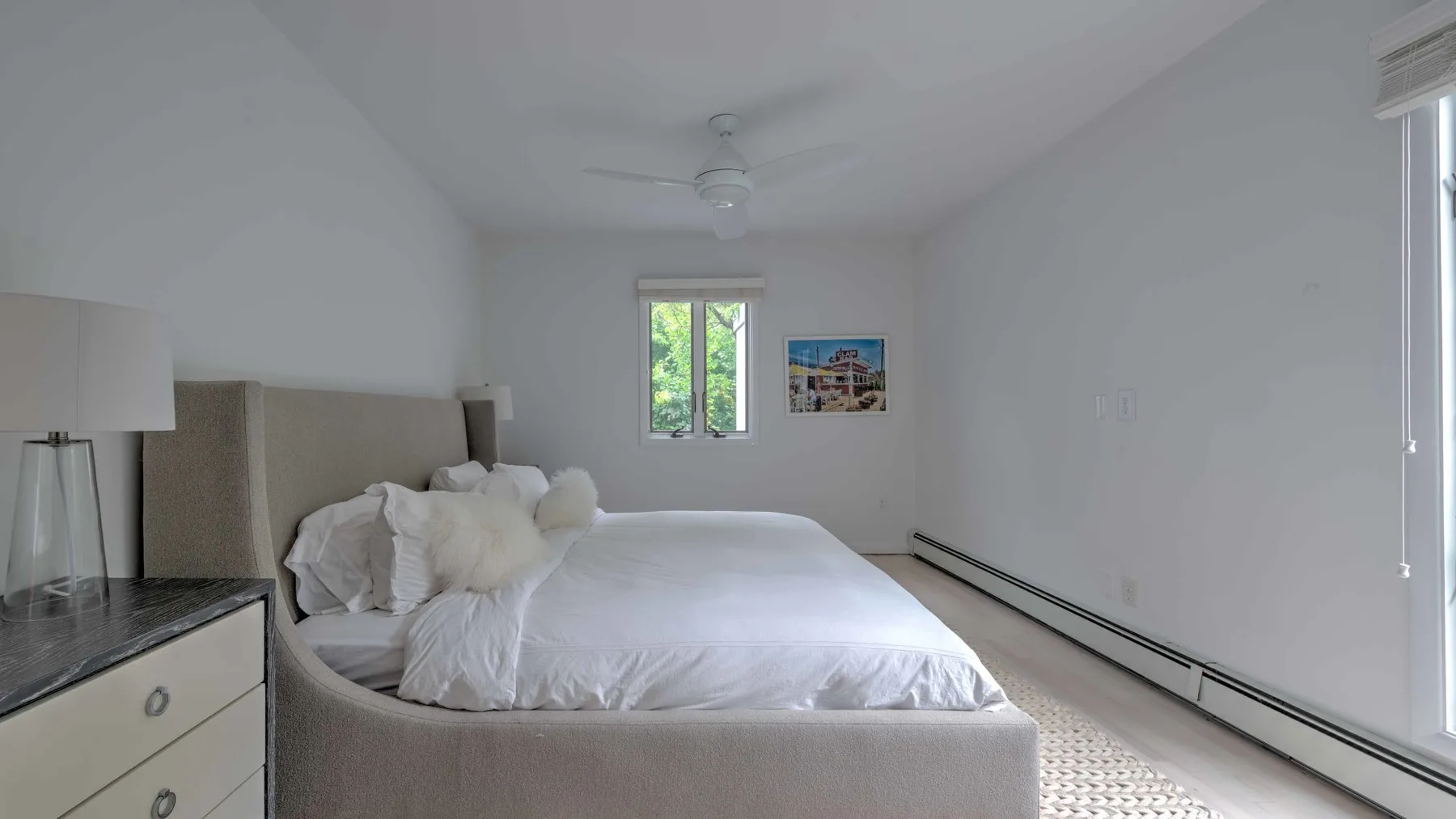 A bright bedroom with a neatly made bed and a window overlooking greenery.