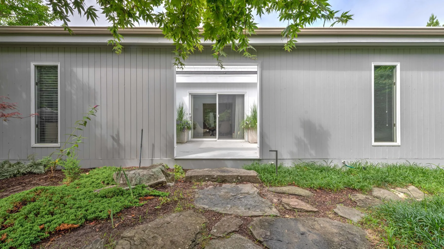 A modern house exterior with a central entrance opening onto a stone path.