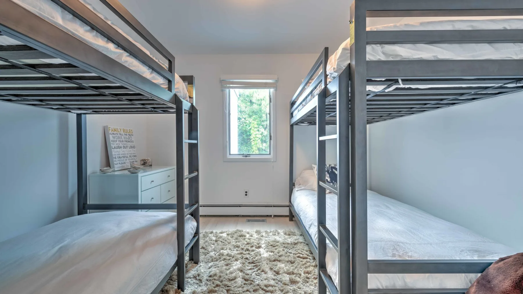 A bedroom with bunk beds on either side of a window and a rug.
