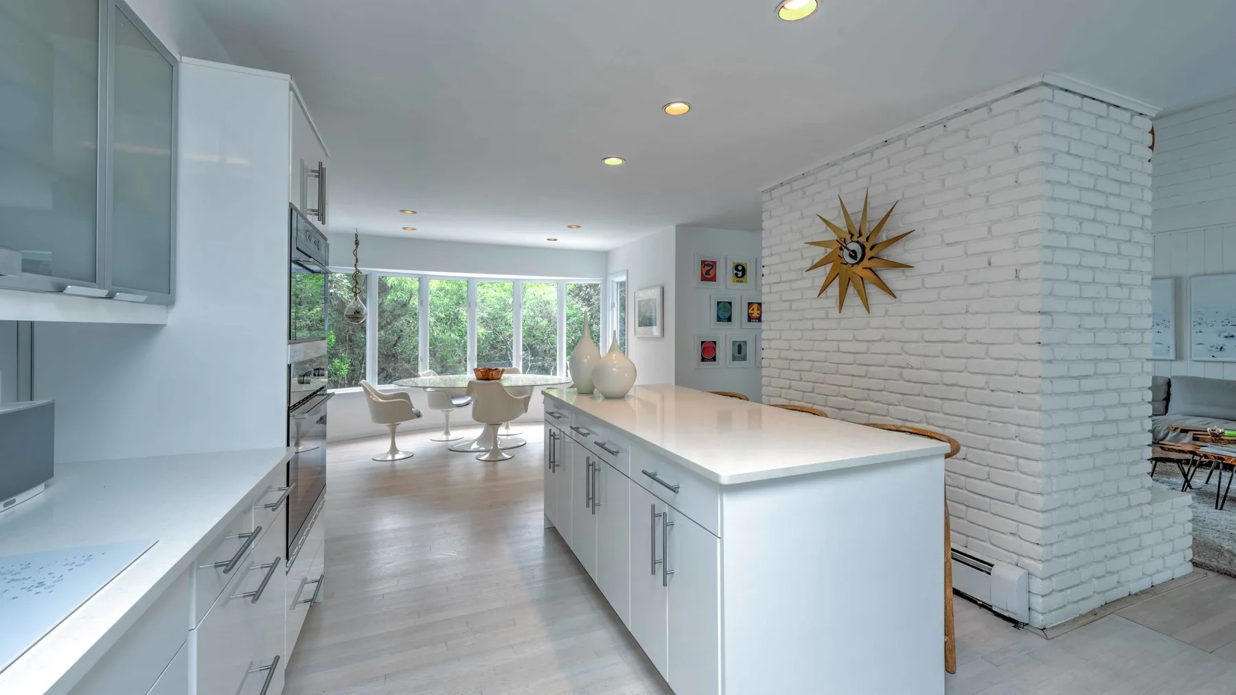 A bright modern kitchen with white cabinetry and a central island opens onto a dining area.