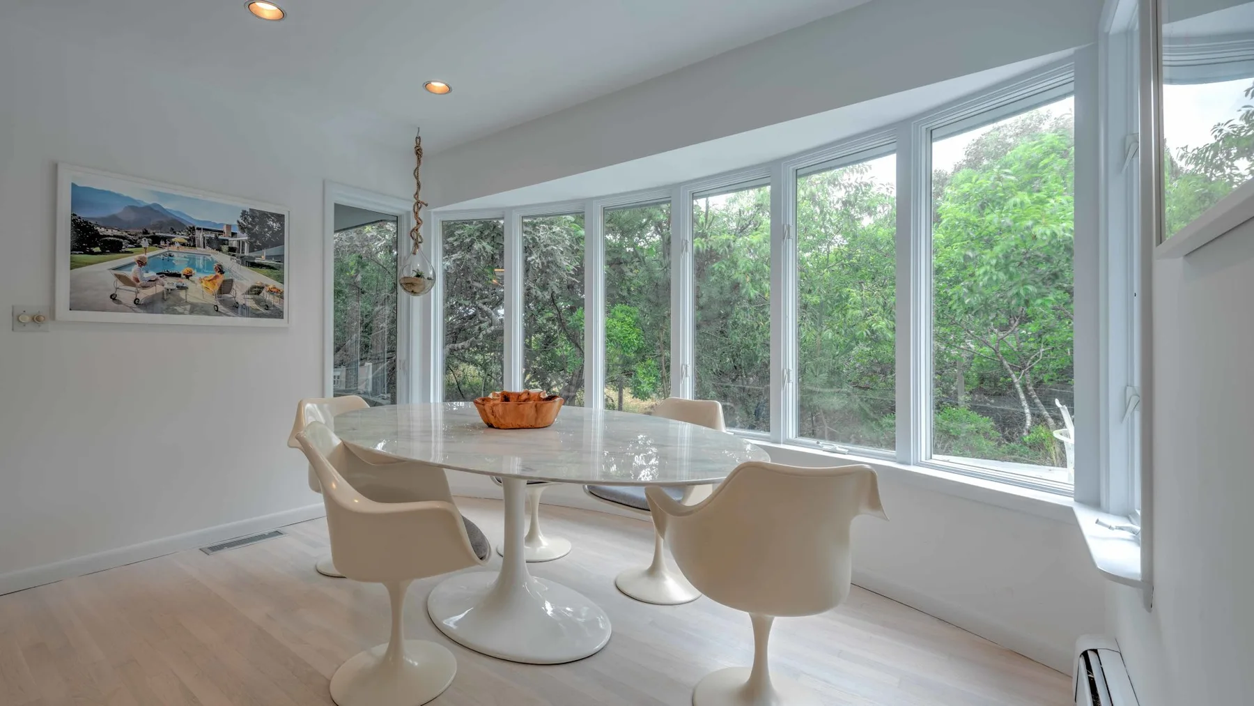 Un comedor luminoso con una mesa blanca junto a grandes ventanas con vistas a la vegetación.