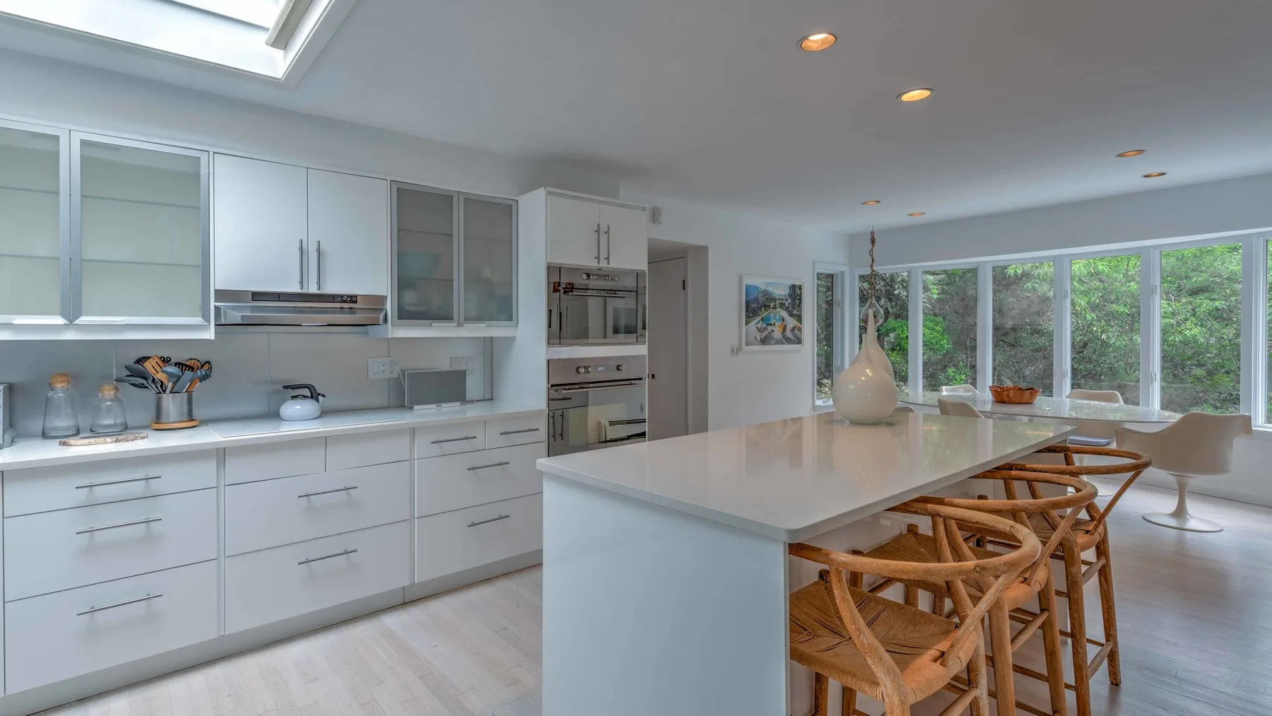 A bright modern kitchen with a large island and wooden seating beside wide windows.