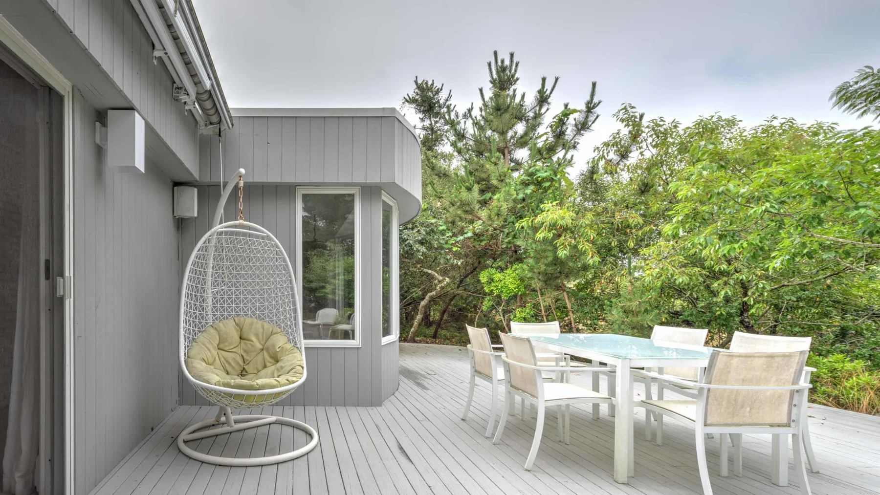 An outdoor dining area on a wooden deck, with a table and chairs beside a hanging seat.