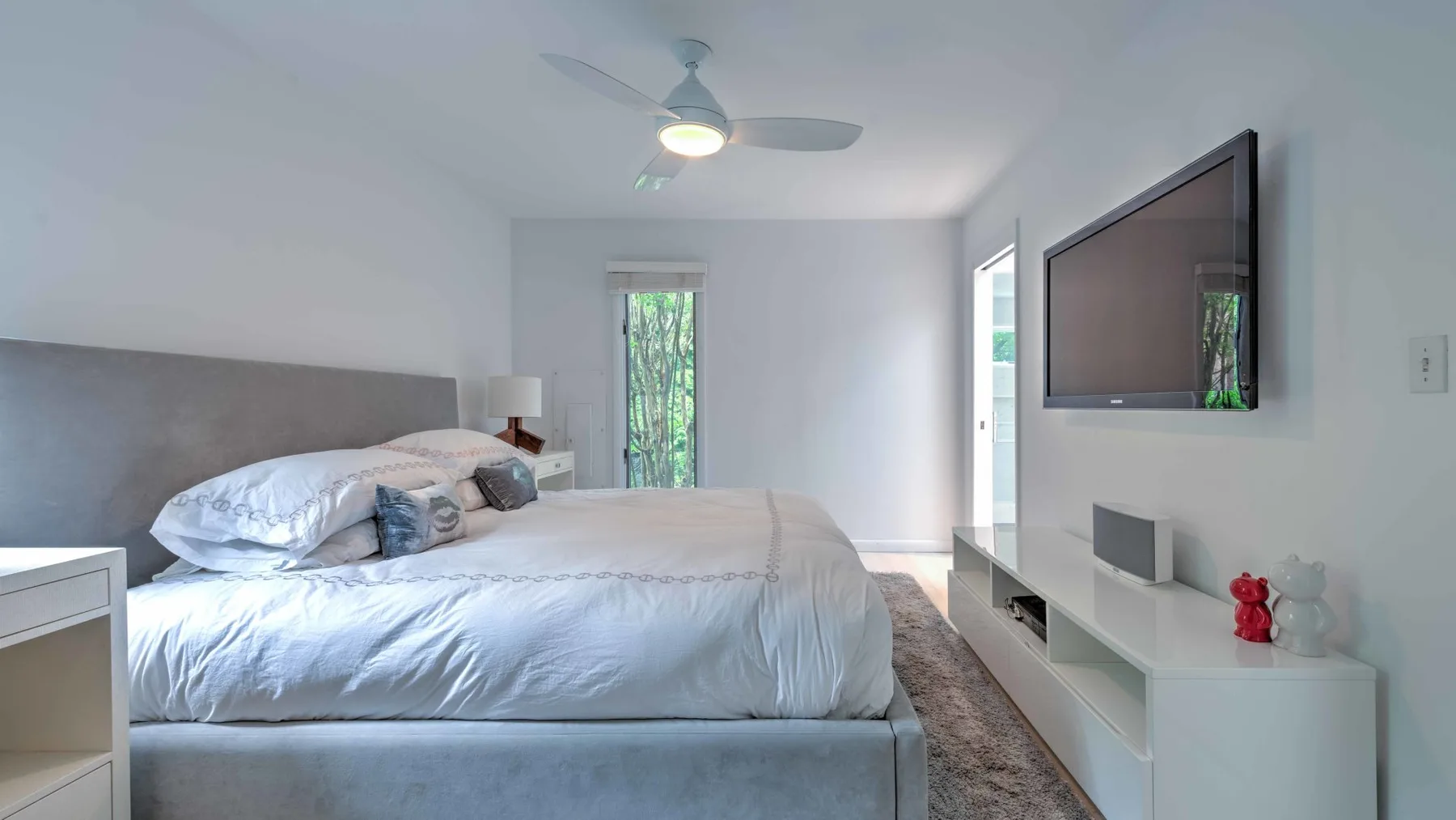 A bright bedroom with a neatly made bed and a wall-mounted television.