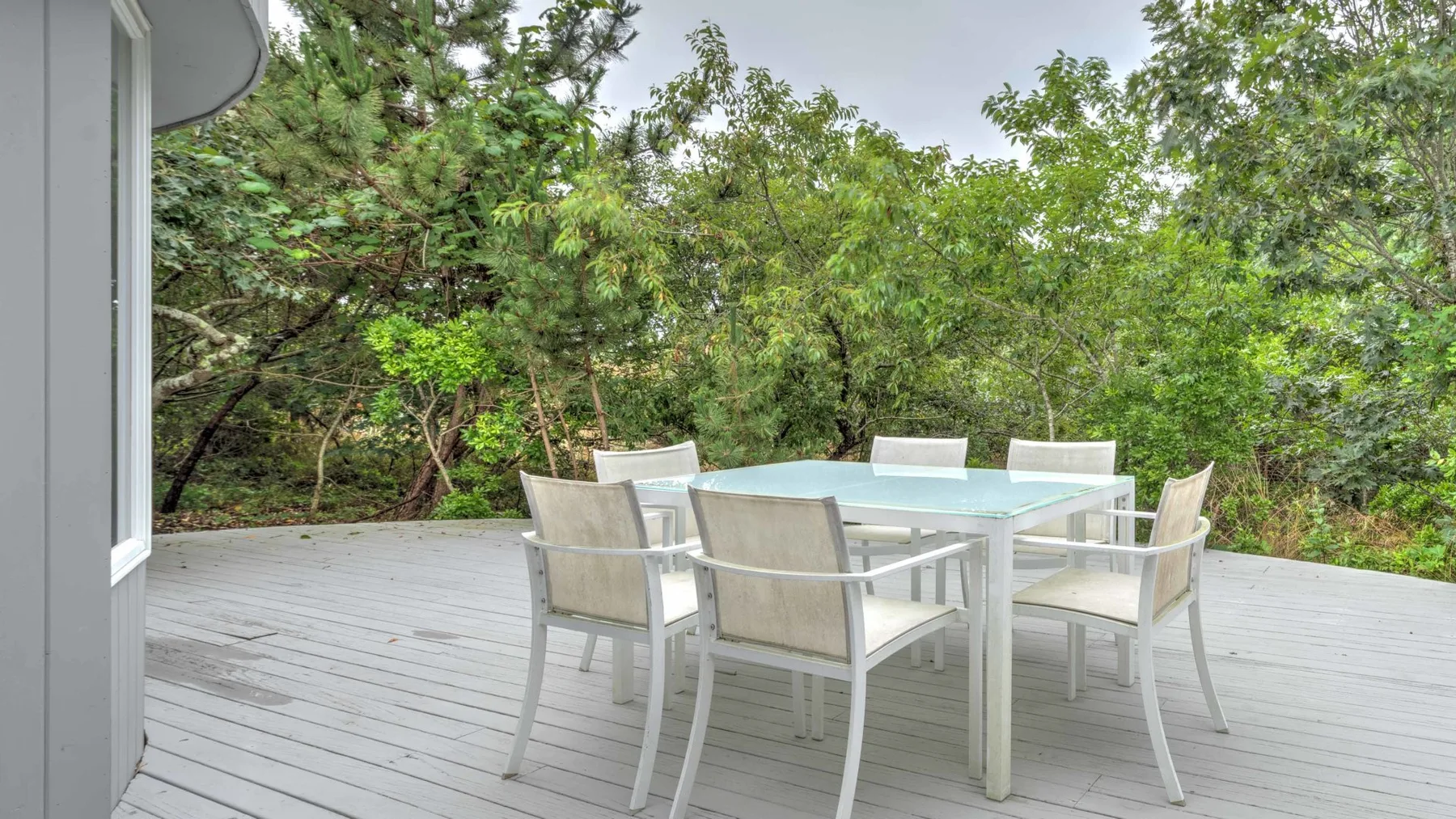 An outdoor dining area with a table and chairs on a deck surrounded by trees.